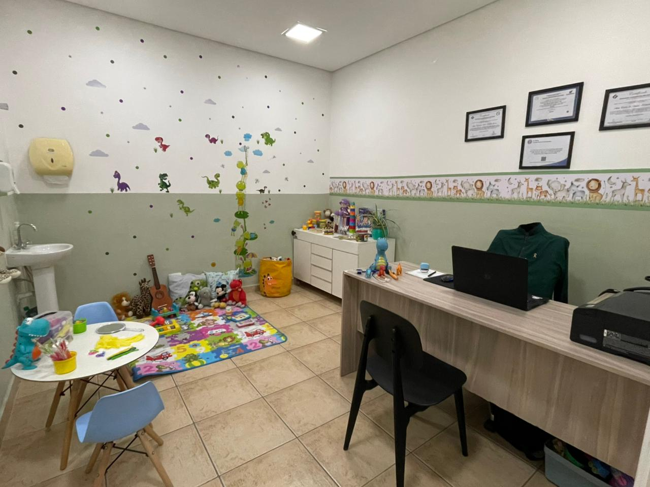 Sala de atendimento com mesa, brinquedos e certificações